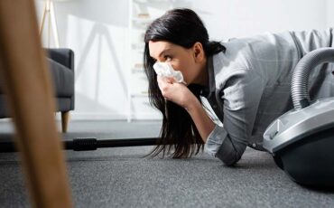 selective focus of allergic woman covering mouth with napkin and holding vacuum cleaner