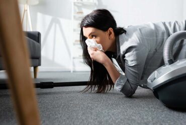 selective focus of allergic woman covering mouth with napkin and holding vacuum cleaner